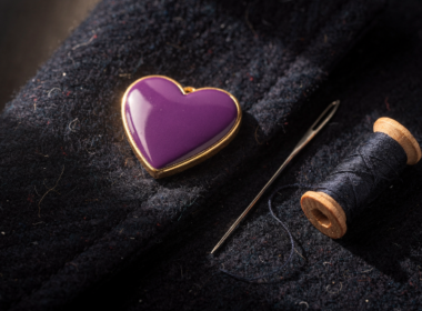 Purple Heart Day medal with gold trim resting on a folded navy wool coat beside a sewing needle and thread