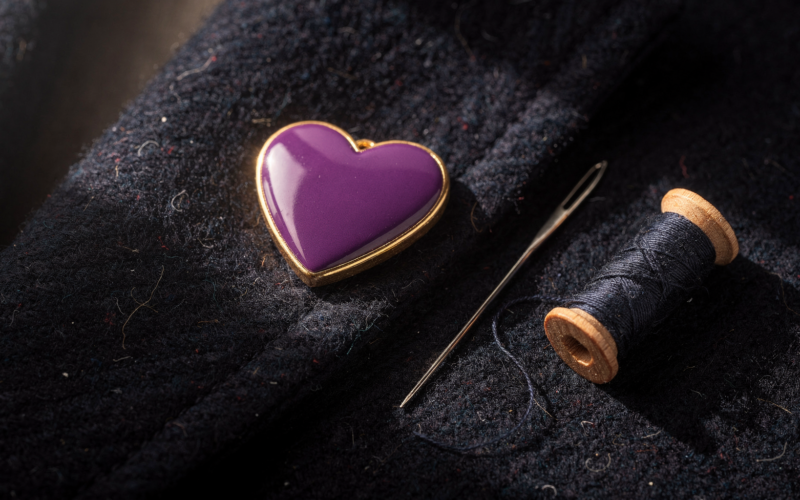 Purple Heart Day medal with gold trim resting on a folded navy wool coat beside a sewing needle and thread