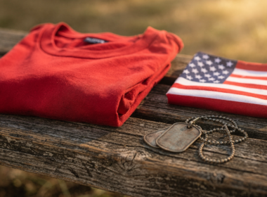 RED Friday meaning shown by a folded red t shirt on a wooden bench beside a small folded American flag and dog tags