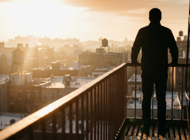 Silhouette of a figure on a fire escape looking out over a golden hazy city skyline