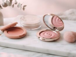 Rare Beauty concept: blush compacts and a makeup brush on marble in soft pink light