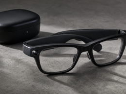 Smart glasses with a small camera lens and a speaker arm resting on a concrete surface