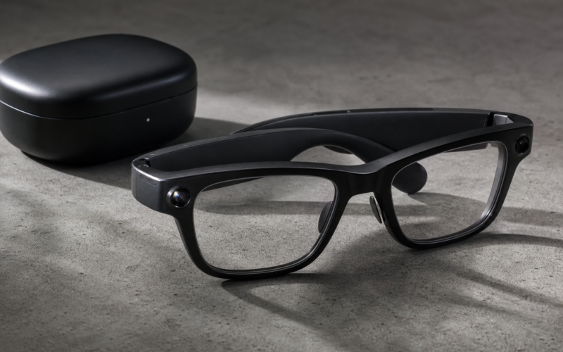 Smart glasses with a small camera lens and a speaker arm resting on a concrete surface