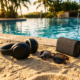 Headphones and sunglasses on bright sand beside a poolside speaker in golden summer light