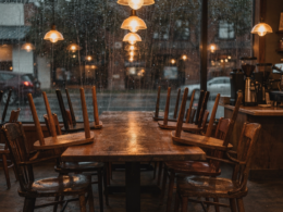 Empty neighborhood coffee shop after closing with chairs upturned on tables and warm pendant lights on, illustrating disappearing third places