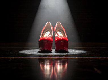 Low angle view of scarlet patent platform heels lit by a hard theatrical spotlight