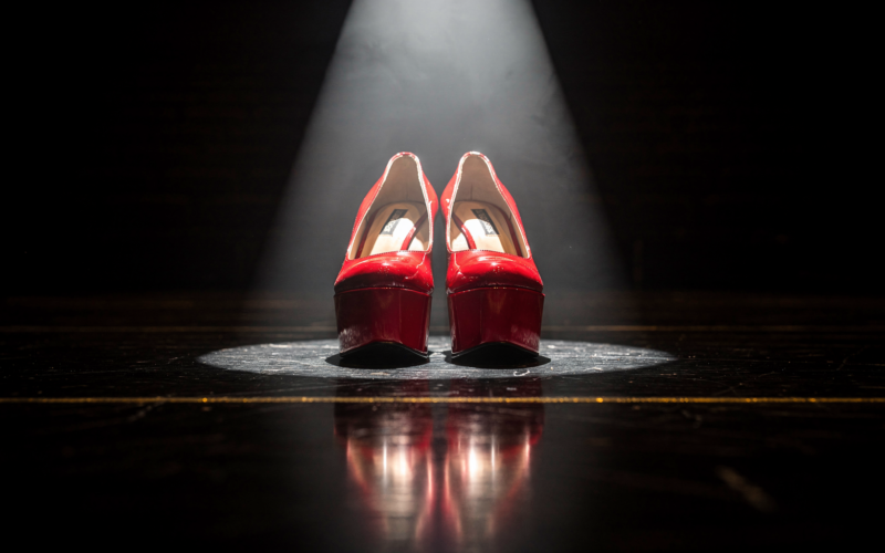 Low angle view of scarlet patent platform heels lit by a hard theatrical spotlight
