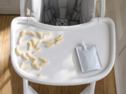 A high chair tray with puffed snacks and an unlabeled pouch representing ultra processed toddler foods