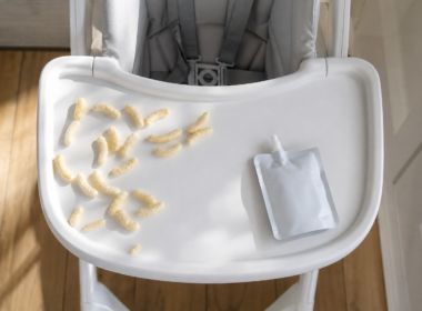 A high chair tray with puffed snacks and an unlabeled pouch representing ultra processed toddler foods
