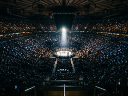 Packed arena seen from the upper bowl with a single brightly lit octagon at the center