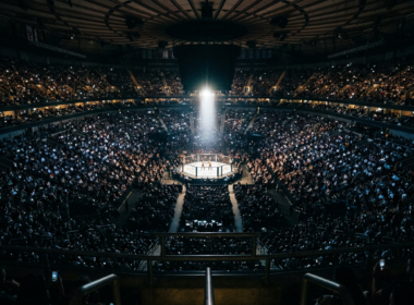 Packed arena seen from the upper bowl with a single brightly lit octagon at the center