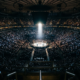 Packed arena seen from the upper bowl with a single brightly lit octagon at the center