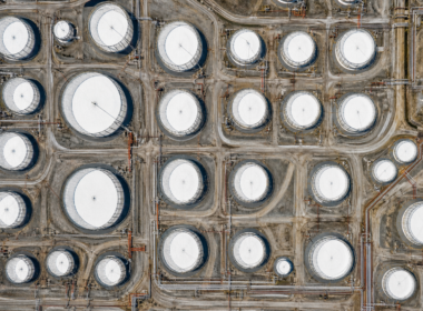 Aerial view straight down over rows of circular white oil storage tanks in bright midday sun