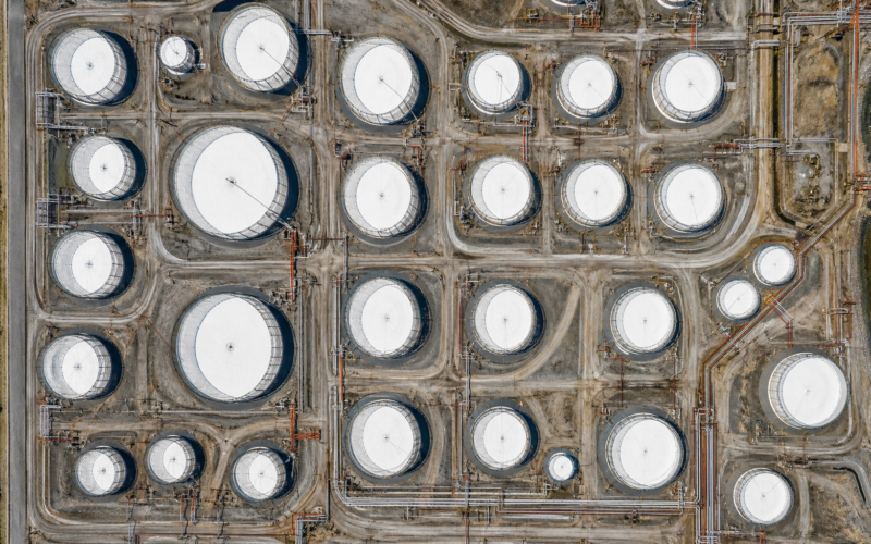Aerial view straight down over rows of circular white oil storage tanks in bright midday sun