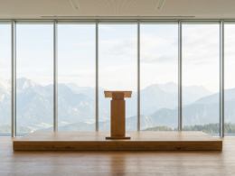 Empty wooden lectern on a stage before a full height window wall looking out at mountains