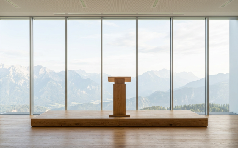 Empty wooden lectern on a stage before a full height window wall looking out at mountains