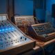 William Orbit tribute image of a vintage analog synthesizer and mixing console in a dimly lit recording studio