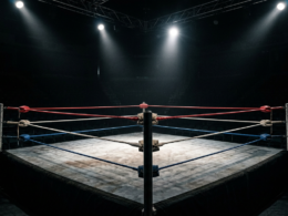 An empty wrestling ring under dramatic spotlights in a dark arena