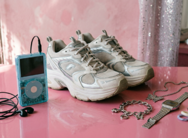 Retro early 2000s objects including a translucent music player and chunky sneakers on a glossy pink surface